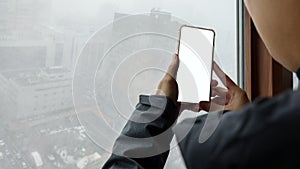 Woman hand holding mobile phone with blank white screen mockup near window at outside a snowy