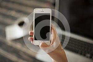 Woman hand holding mobile phone, and laptop and coffee cup in ba