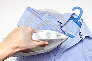 Woman hand holding a modern electrical white iron, a blue shirt on background, close up view - ironing, laundry and housework