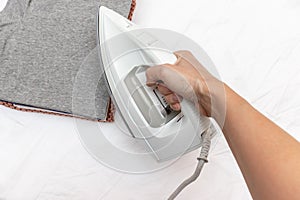 Woman hand holding a modern electrical white iron, a stack of clothes on background, close up view - ironing, laundry and