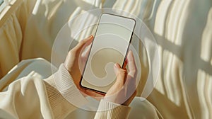 Woman hand holding a modern frameless smartphone with blank white screen on background of a modern interior
