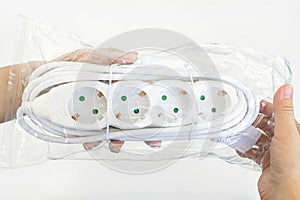 Woman hand holding new four outlets power extension cord in a transparent plastic pakage over white table. Electric power strip