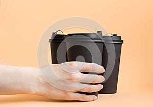 Woman hand holding one black take away coffee cup on neutral pastel background.