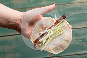 Woman hand holding pancake with Pekin Duck meat, onions and cucumbr pieces. Top view