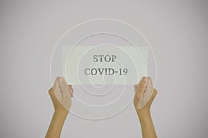 Woman hand holding paper card with stop covid-19 text.