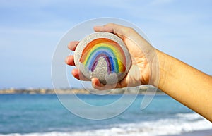Woman hand holding pebble with painted rainbow
