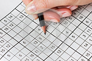 Woman hand holding a pencil and solves crossword sudoku