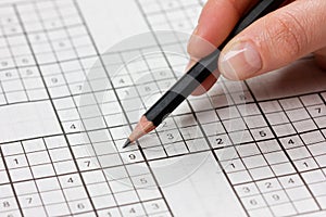 Woman hand holding a pencil and solves crossword sudoku