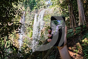 Woman hand holding a phone making a photograph of a waterfall