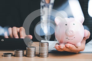 Woman hand holding piggy bank with money stack step up growing growth on wood table