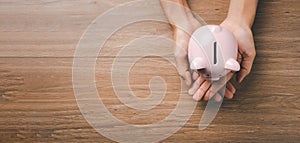 Woman hand holding piggy bank on wooden background