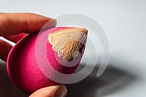 Woman hand holding pink beauty blender with the beige liquid foundation on it - Image