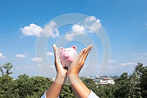 Woman Hand holding pink piggy bank with blue sky background, step up growing business to success and saving for retirement concept