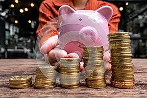 Woman hand holding pink piggy bank with golden coins growth bar graph, step up growing business to success and saving for