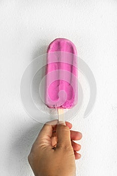 Woman hand holding pink stick ice scream for summer refreshment on white concrete wall background