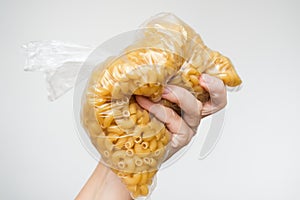 Woman hand holding a plastick bag full of raw pasta against white background, carbohodrates and flour