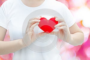 Woman hand holding plush a red heart at left her chest on pink background