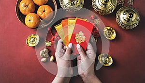 Woman hand holding pow or red packet, orange and gold ingots on a red background