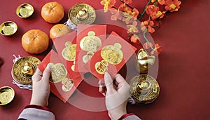 Woman hand holding pow or red packet, orange and gold ingots on a red background