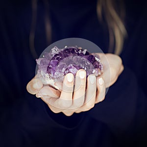 Woman hand holding purple crystal, amethyst, melancolic sensual studio shot
