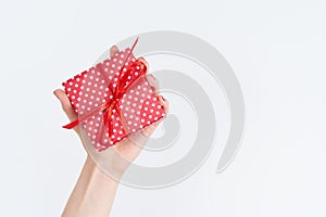 Woman hand holding red gift with ribbon, manicured hand with nail polish on white background with copy space