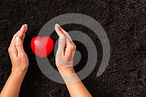 Woman hand holding red heart on compost fertile black soil