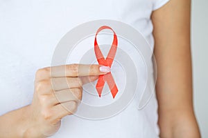 Woman hand holding red ribbon HIV, world AIDS day awareness ribbon.