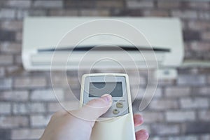 Woman hand holding a remote control directed on air conditioner.