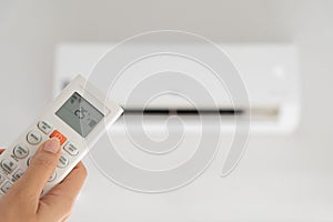 Woman hand holding remote controller directed on the air conditioner inside the room and set at ambient temperature,25 degrees