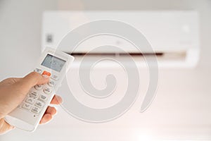 Woman hand holding remote controller directed on the air conditioner inside the room and set at ambient temperature,25 degrees