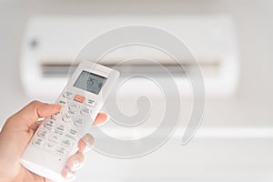 Woman hand holding remote controller directed on the air conditioner inside the room and set at ambient temperature,25 degrees