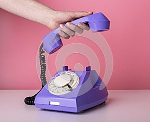 Woman hand holding retro phone handset on pink background. Vintage style