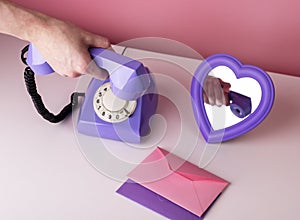Woman hand holding retro phone handset. Vintage style telephone on table with heart-formed mirror and envelopes