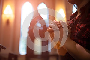 Woman hand holding rosary against cross and praying to God at church