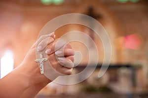 Woman hand holding rosary against cross and praying to God at church