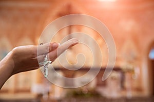 Woman hand holding rosary against cross and praying to God at church