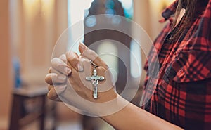 Woman hand holding rosary against cross and praying to God at church