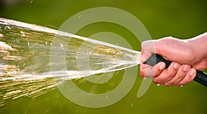 Woman hand holding rubber water hose and using finger