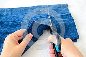 Woman hand holding a scissors and cutting out a folded in half blue jean shorts. Shorten the denim shorts with scissors and sewing