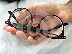 Woman hand holding shortsighted or nearsighted eyeglasses on white pillow, white bed background, Close up, Optical concept