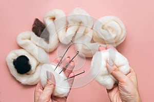 woman hand holding skein of wool and needle felting kit. felted woolen wool on pink background, handicraft from above