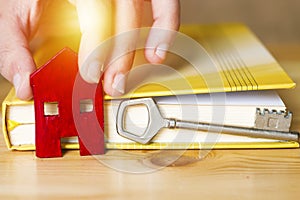 Woman hand holding small red house with key and book, sell house business concept