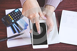 Woman hand holding smart phone calculating her monthly expenses with credit card,saving account book, deadline calendar concept fo