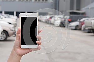 Woman hand holding smartphone in car parking area