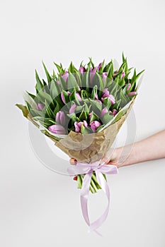 Woman hand holding soft lilac tulips flowers on white background. bouquet decorated with kraft paper