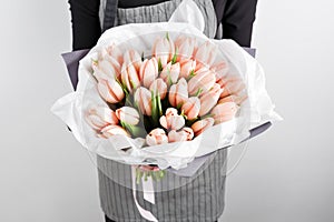 Woman hand holding soft pink tulips flowers on white background. bouquet decorated with kraft paper