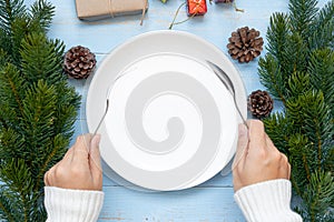 Woman hand holding spoon and fork over Empty plate with Christmas decoration, preparation for Happy New Year and Xmas