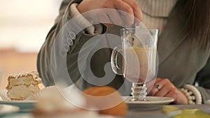 Woman hand holding spoon and stirring coffee latte at table with sweet cake