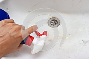 Woman hand holding a sprayer cleaning agent for wasing old dirty washbasin with rust stains, limescale and soap stains in the