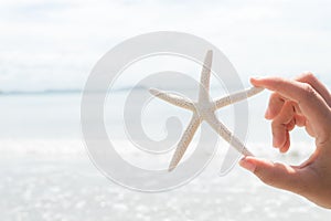 Woman hand holding starfish over sea and Sandy beach